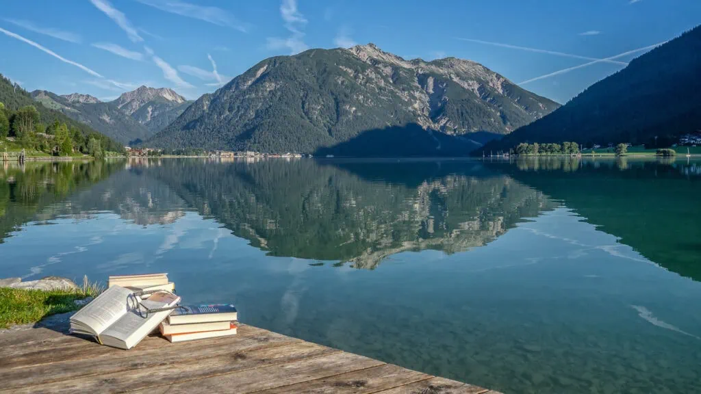 Bücher und Brille auf Holzsteg vor idyllischem Bergpanorama.